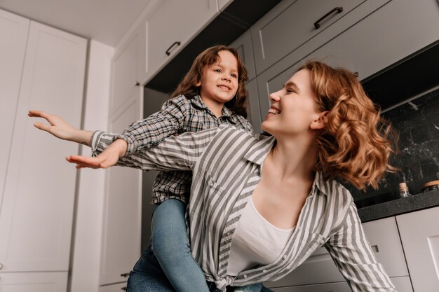 La donna con i capelli mossi gioca con la figlia e si pone come aeroplani.