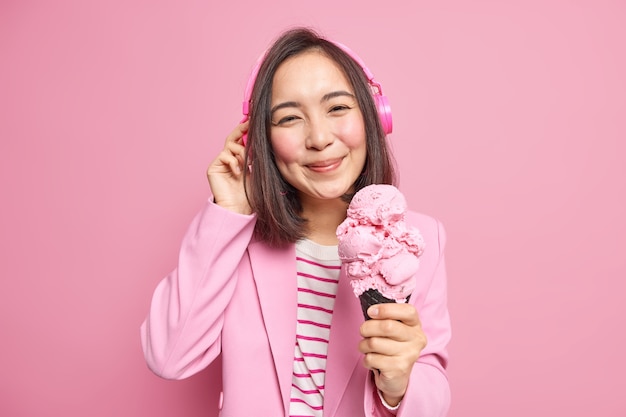 la donna con i capelli scuri ascolta musica tramite le cuffie vestita con abiti alla moda mangia deliziose pose di gelato a cono