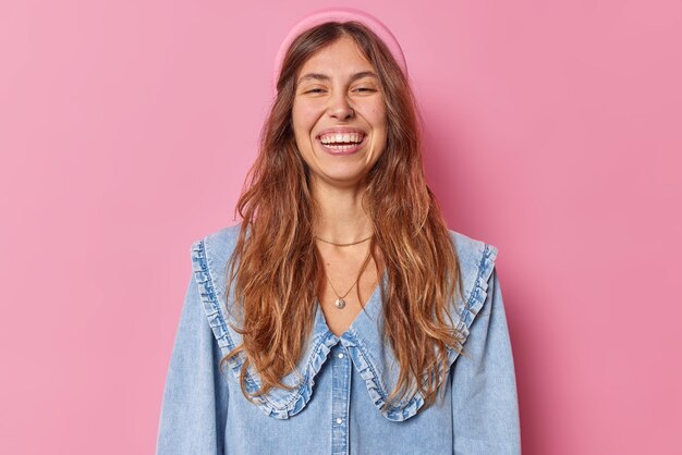 la donna con un ampio sorriso mostra denti bianchi perfetti indossa una camicia di jeans e una fascia isolata sul rosa ha un piercing nel naso mostra emozioni felici. Foto in studio