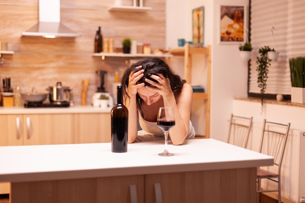 La donna con una bevanda alcolica sta bevendo da sola una bottiglia di vino che le fa venire i postumi di una sbornia