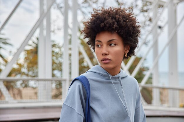 la donna concentrata lontano dai pensieri indossa una felpa casual pone passeggiate all'aperto in città. Stile di vita delle persone e tempo libero