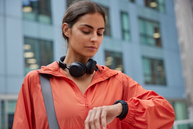 la donna controlla il tempo sullo smartwatch usa le cuffie per ascoltare la traccia audio vestita in giacca aspetta le pose dell'allenatore