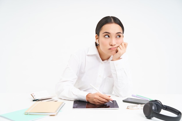 La donna coreana stanca e annoiata nell'impiegato d'ufficio si siede con il tablet digitale ascolta la musica negli auricolari