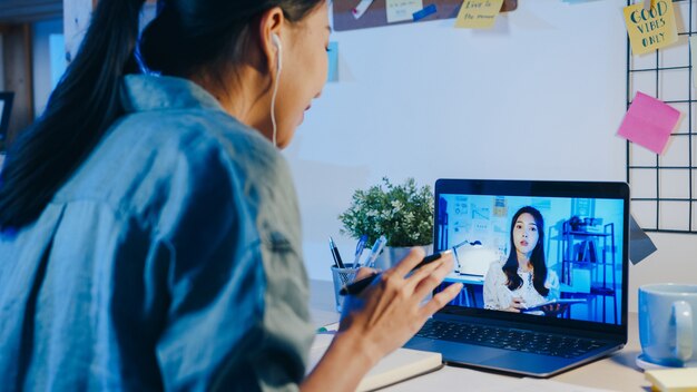 La donna d'affari asiatica che utilizza il laptop parla con i colleghi del piano in una riunione di videochiamata in soggiorno.