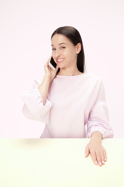 La donna d'affari felice seduta con il telefono cellulare contro il rosa.