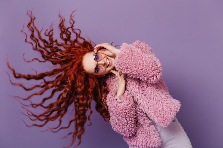 Foto gratuito la donna dagli occhi azzurri con gli occhiali lilla balla e gioca con i suoi capelli. immagine della ragazza in cappotto rosa su uno spazio isolato.