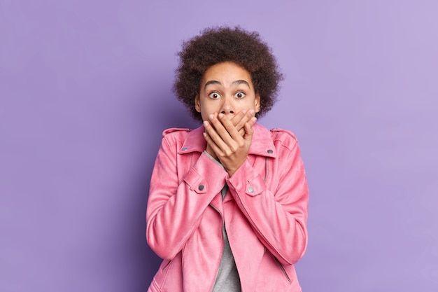 La donna dai capelli ricci scioccata copre la bocca e guarda con paura nota che qualcosa di orribile indossa un'elegante giacca rosa