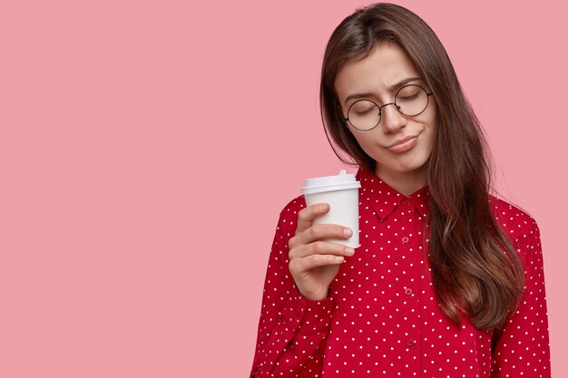 La donna dai capelli scuri oberati di lavoro ha un aspetto assonnato, porta il caffè da asporto nelle mani, fa un sonnellino durante la pausa, vestito con un vestito elegante