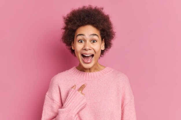 La donna dalla pelle scura positiva indica se stessa con un'espressione felicissima ha uno sguardo divertente