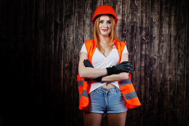 La donna dell'ingegnere in arancione protegge il casco e la giacca da costruzione su sfondo di legno