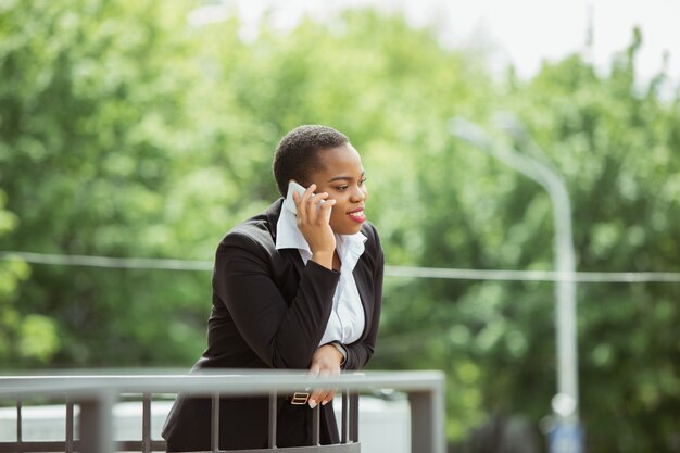 La donna di affari afroamericana in abbigliamento dell'ufficio che sorride, sembra sicura e felice, occupata