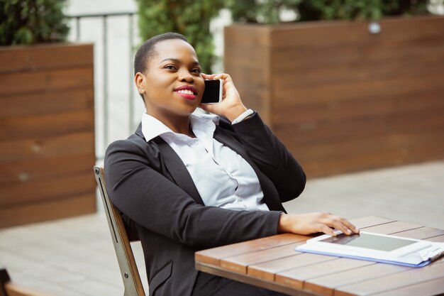 La donna di affari afroamericana in abbigliamento dell'ufficio che sorride, sembra sicura e felice, occupata