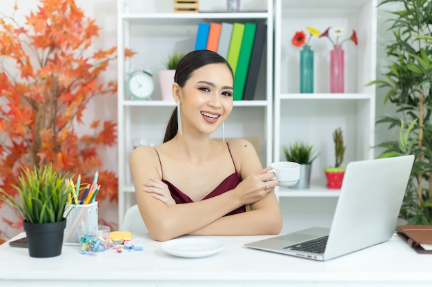 La donna di affari asiatica prende una pausa caffè dopo il lavoro al computer portatile sullo scrittorio