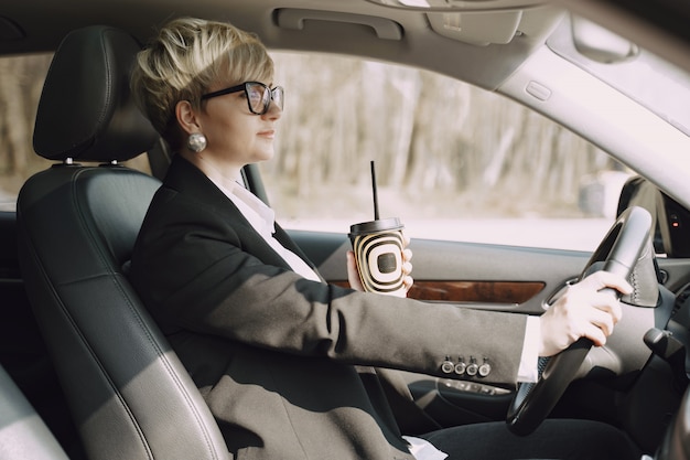 La donna di affari che si siede dentro un'automobile e beve un caffè
