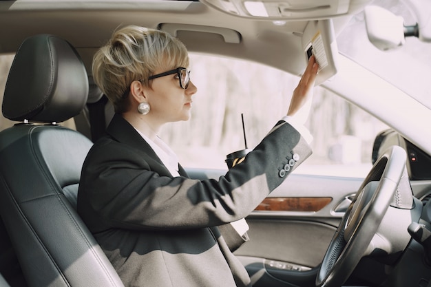 La donna di affari che si siede dentro un'automobile e beve un caffè