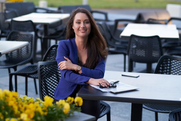 La donna di affari sorridente allegra sta lavorando ai suoi documenti fuori dal suo ufficio. È seduta in un piccolo caffè.