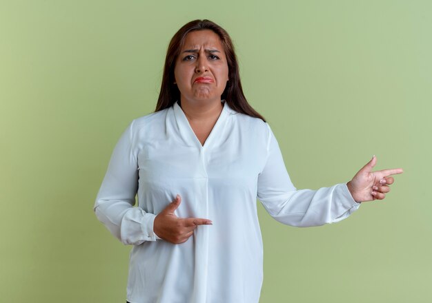 La donna di mezza età caucasica casuale triste indica al lato isolato sulla parete verde oliva con lo spazio della copia