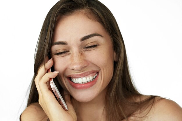 La donna di risata graziosa parla sul telefono che sta sul fondo bianco
