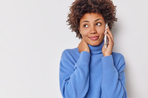 la donna distoglie lo sguardo con un'espressione soddisfatta fa una telefonata vestita con un dolcevita blu casual isolato su uno spazio bianco per la copia dell'annuncio