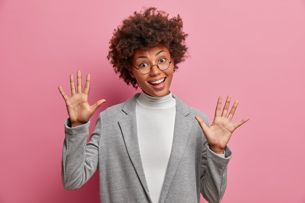 La donna divertente con i capelli ricci solleva i sorrisi delle palme positivamente