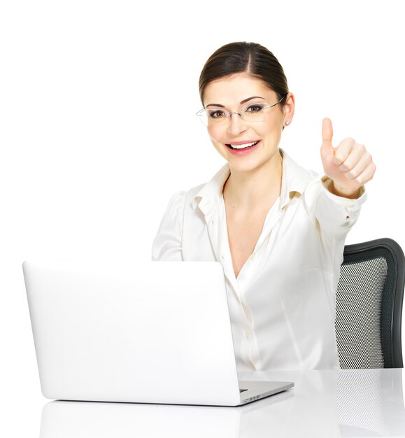 La donna e il computer portatile con i pollici aumentano il segno in camicia bianca dell'ufficio - isolata su fondo bianco.