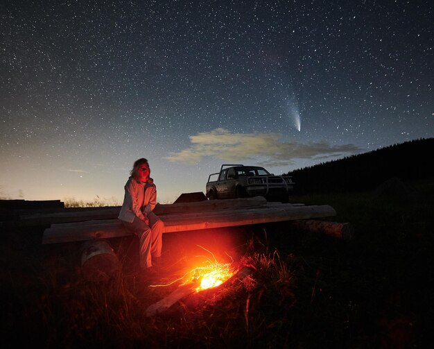 La donna è seduta vicino al falò in montagna di notte