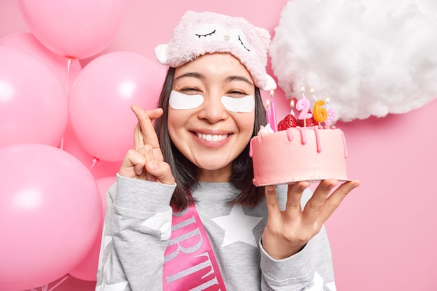 la donna esprime un desiderio prima di soffiare le candeline sulla torta di compleanno incrocia le dita sorride felice vestita in pigiama festeggia il compleanno