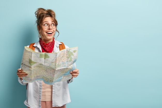 La donna europea allegra ha un viaggio interessante, guarda da parte, tiene la mappa, controlla il percorso o la posizione, viaggia in una città turistica