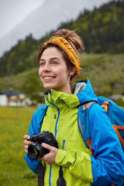 La donna europea spensierata sorridente tiene la macchina fotografica professionale, guarda positivamente in lontananza