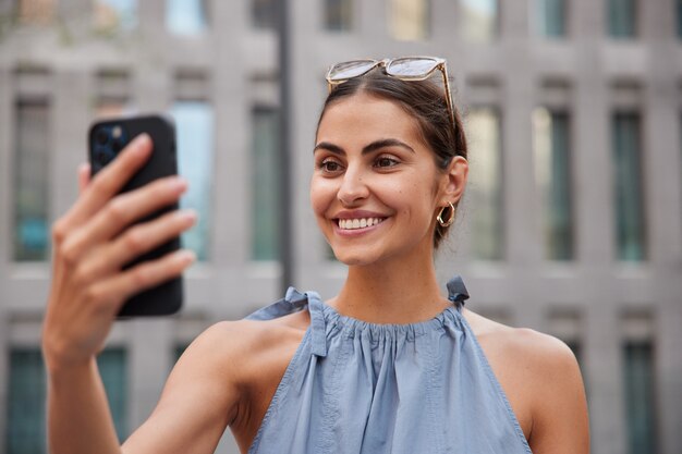 la donna fa una videochiamata tramite smartphone mentre passeggia in un ambiente urbano gode di una giornata estiva ha pose di umore ottimista contro sfocato