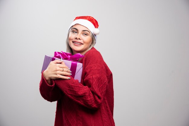 La donna felice in cappello della Santa abbraccia il regalo di Natale.