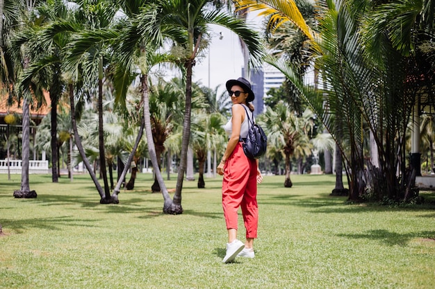 La donna felice viaggia intorno a Bangkok con lo zaino, godendo della bella giornata di sole nel parco tropicale sul campo di erba verde