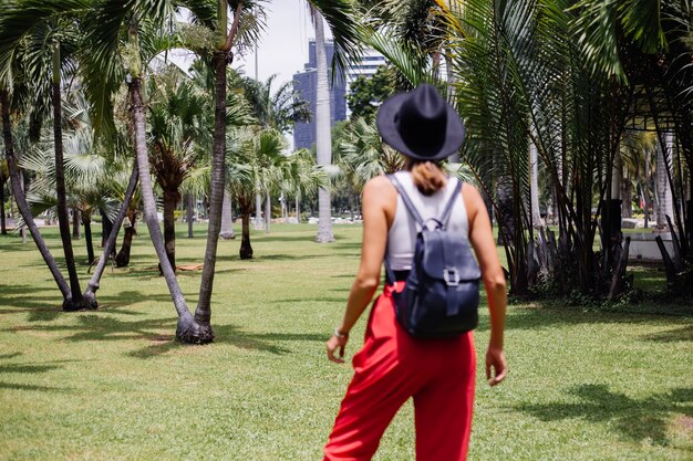 La donna felice viaggia intorno a Bangkok con lo zaino, godendo della bella giornata di sole nel parco tropicale sul campo di erba verde