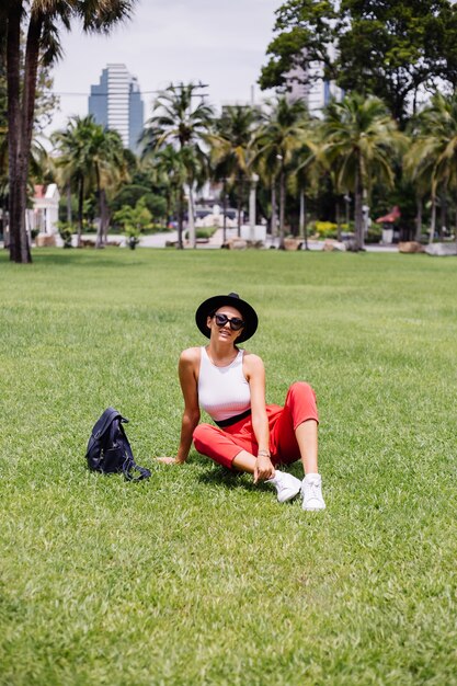 La donna felice viaggia intorno a Bangkok con lo zaino, godendo della bella giornata di sole nel parco tropicale sul campo di erba verde