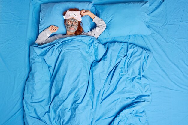 la donna giace in un letto comodo sotto la coperta applica la maschera facciale indossa la maschera per dormire e il pigiama si sente sola