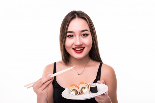 La donna graziosa con capelli neri e le labbra rosse assaggia i rotoli di suushi che tengono le bacchette di legno in sua mano