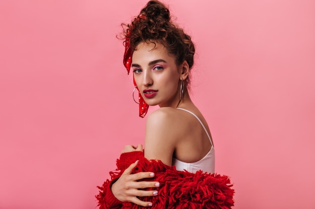 La donna graziosa con il bello trucco esamina la macchina fotografica sul colore rosa