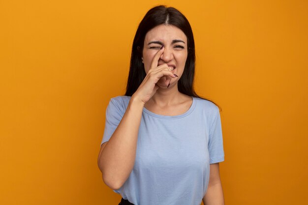 La donna graziosa del brunette dispiaciuta mette la mano sul naso isolato sulla parete arancione