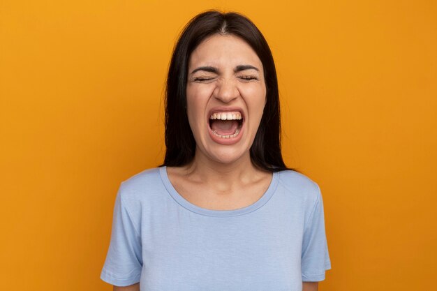 La donna graziosa del brunette infastidita sta con gli occhi chiusi isolati sulla parete arancione