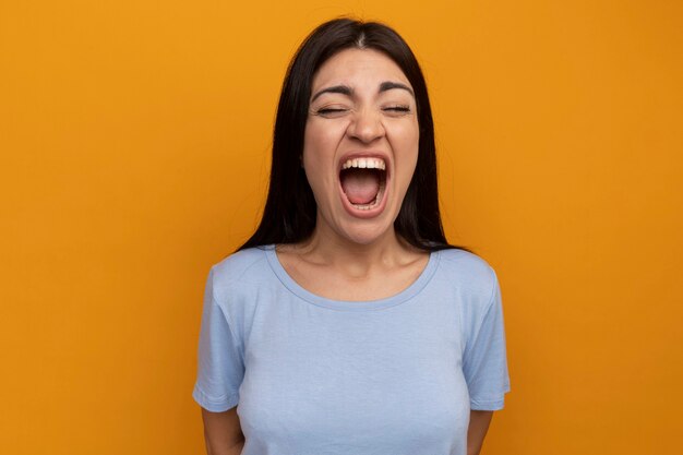 La donna graziosa del brunette infastidita urla isolate sulla parete arancione