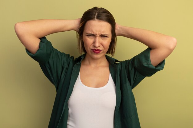 La donna graziosa dispiaciuta mette le mani sulla testa isolata sulla parete verde oliva