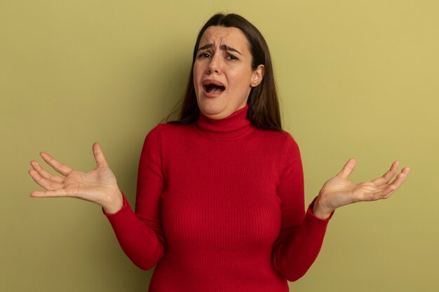 La donna graziosa dispiaciuta tiene le mani aperte isolate sulla parete verde oliva