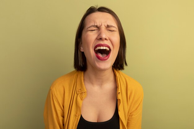 La donna graziosa infastidita sta con gli occhi chiusi isolati sulla parete verde oliva