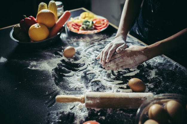 La donna impasta la pasta per fare la pizza su legno. Concetto di cottura.