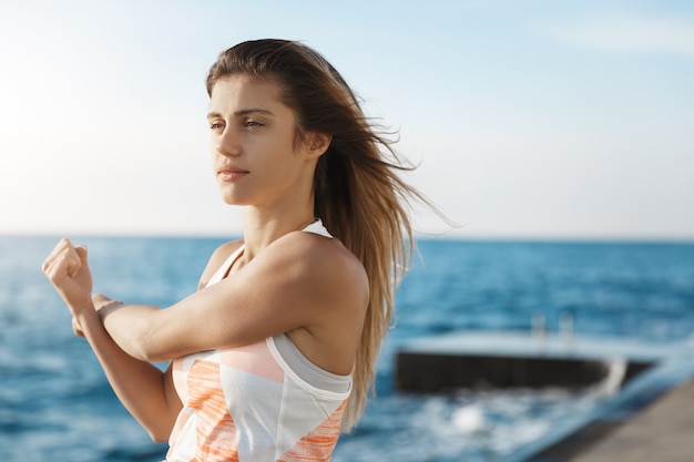 la donna imposta l'obiettivo, mantiene il corpo in forma, allunga le braccia, fa jogging esercizi di riscaldamento dall'aspetto determinato