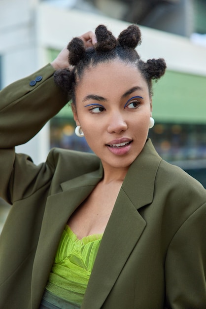 la donna in abiti eleganti indossa orecchini concentrati via ha pose di trucco vivido di acconciatura alla moda. Concetto di moda e moda giovanile