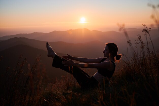 La donna in meditazione è seduta sull'erba in montagna