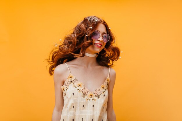 La donna in occhiali da sole e top floreale giallo gioca i capelli su sfondo arancione