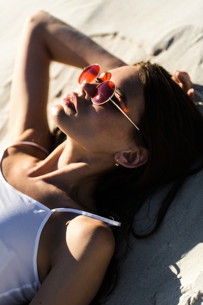 La donna in occhiali da sole rossi si trova su una spiaggia bianca