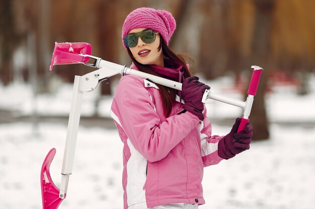 La donna in un parco d'inverno. Signora in tuta sportiva rosa. Donna con scooter da neve.